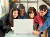 four people standing around looking at a laptop and smiling sort of foolishly