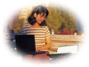 picture of female student sitting on a bench, reading a book and using a laptop
