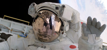 Astronaut Soichi Noguchi waves from the shuttle Discovery payload bay, backdropped by the Earth below – NASA